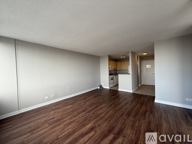 A room with wooden floors and white walls, leading to a kitchen area.