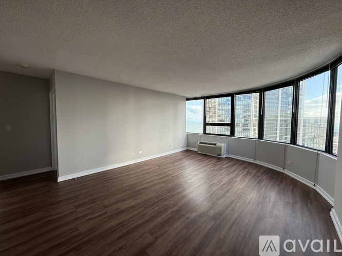 A spacious room with wooden flooring and large windows overlooking a cityscape.