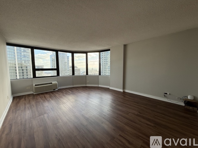 A spacious room with wooden floors and large windows overlooking a cityscape.