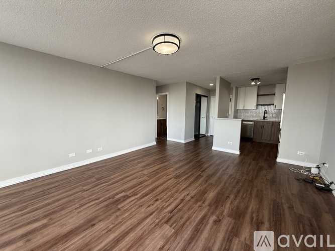 A room with wooden flooring and a kitchen area in the background.