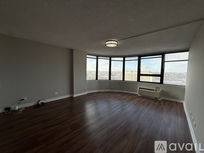 A spacious room with wooden floors and large windows overlooking a cityscape.