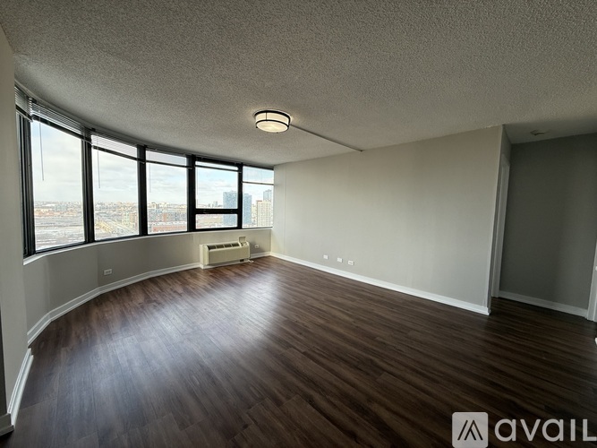 A spacious room with wooden floors and large windows overlooking a cityscape.