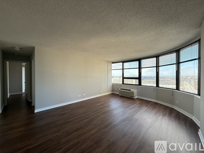 A spacious room with wooden floors and large windows overlooking a cityscape.