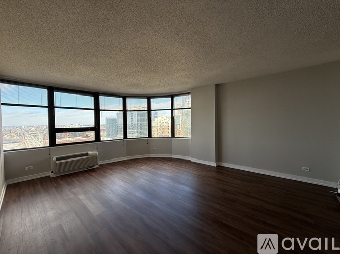 A spacious room with wooden floors and large windows overlooking a cityscape.