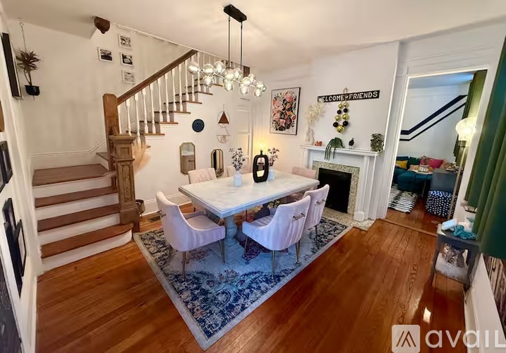 A dining room with a white table and chairs, a staircase, and a fireplace.
