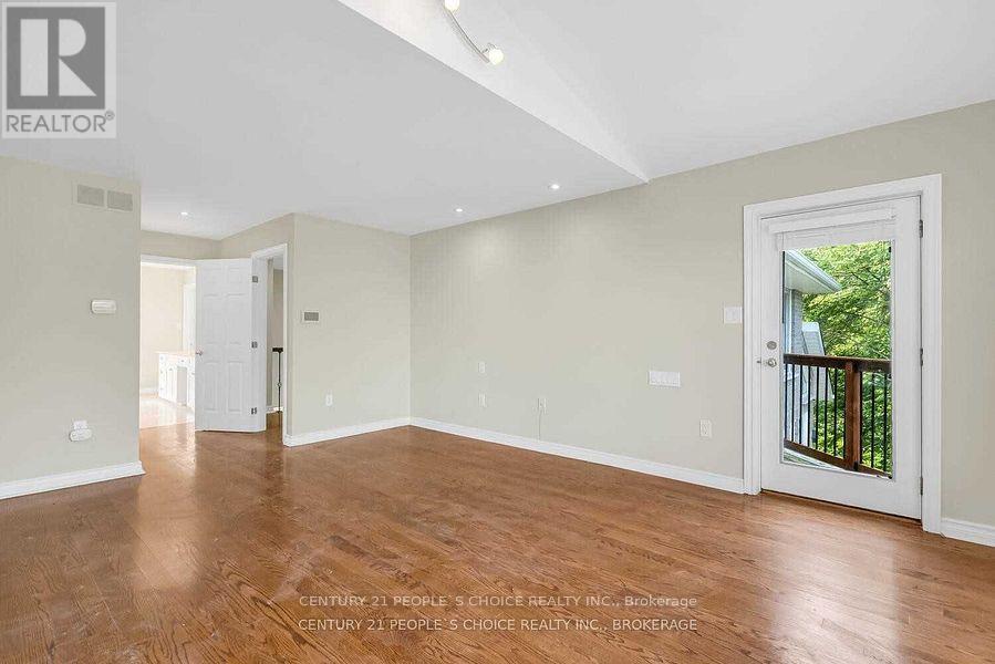 A spacious room with wooden floors and white walls, part of a real estate listing.