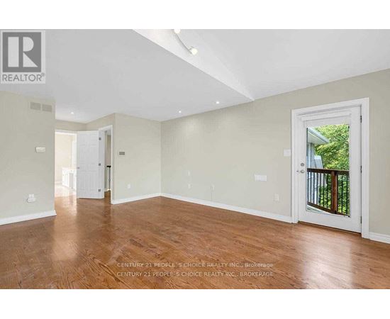 A spacious room with wooden floors and white walls, part of a real estate listing.