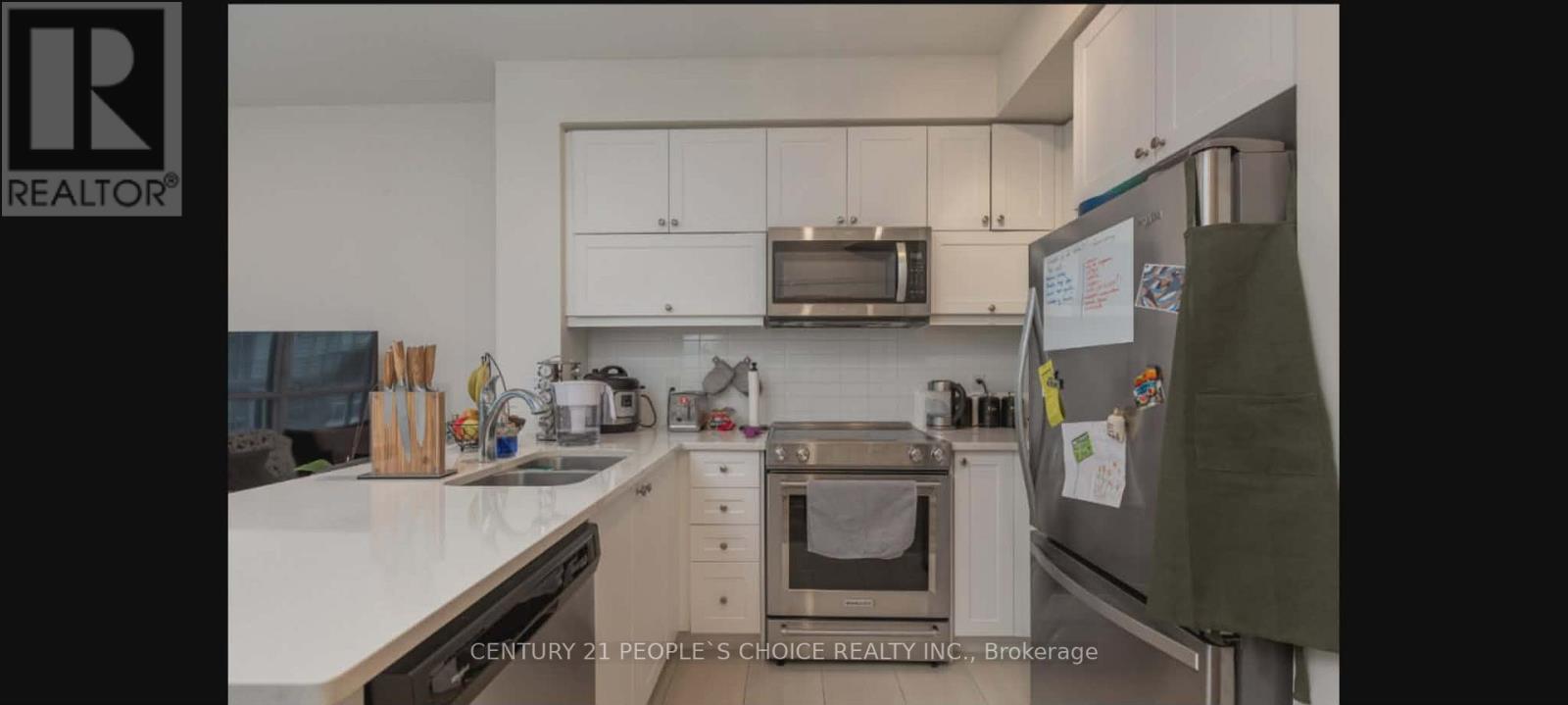 A kitchen with white countertops and a refrigerator with a green towel hanging on it.