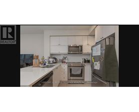 A kitchen with white countertops and a refrigerator with a green towel hanging on it.