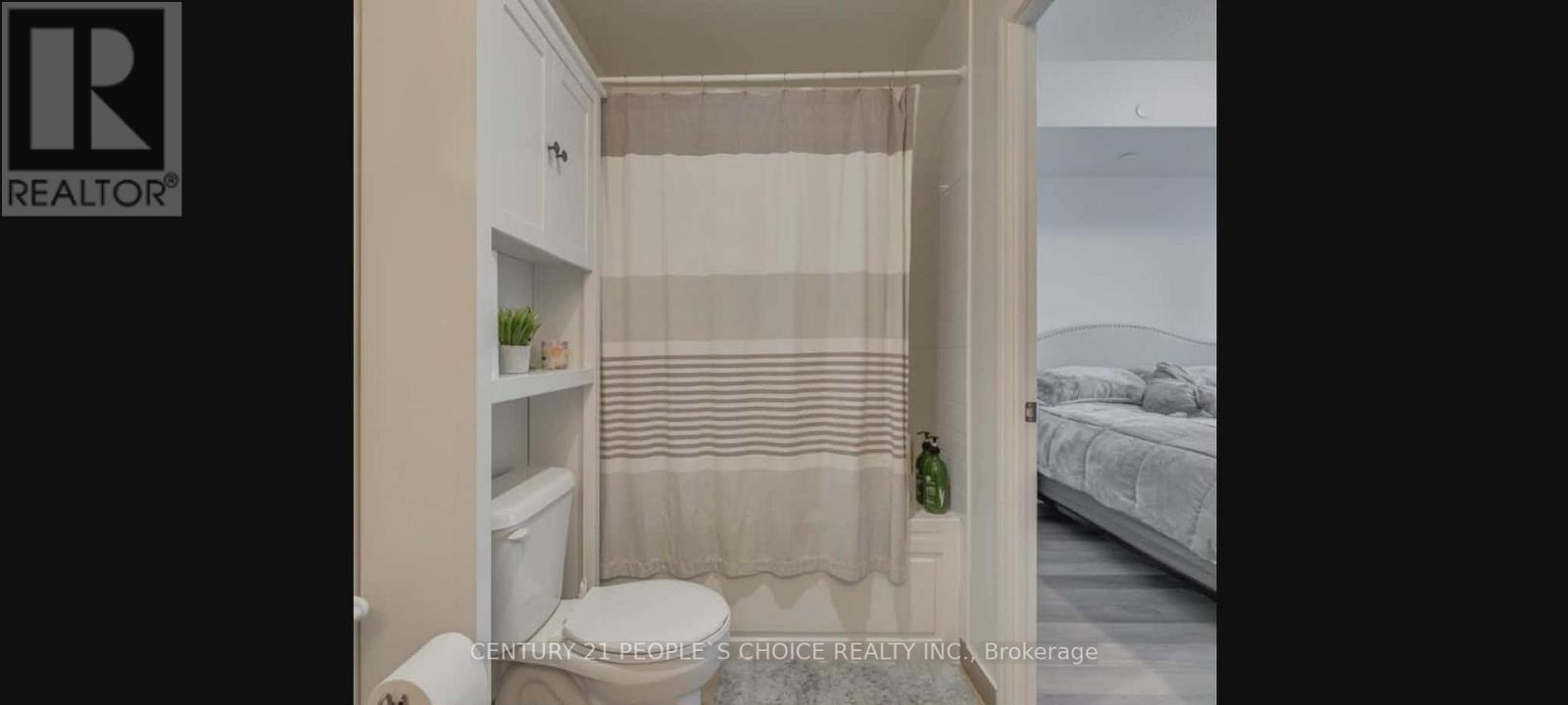 A small bathroom with a toilet, a shower curtain, and a bed in the background.