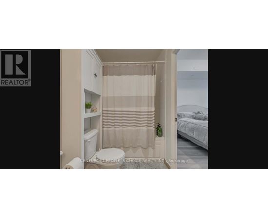 A small bathroom with a toilet, a shower curtain, and a bed in the background.