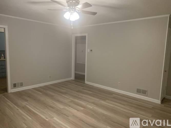 A room with a ceiling fan and light, wooden flooring, and a door.