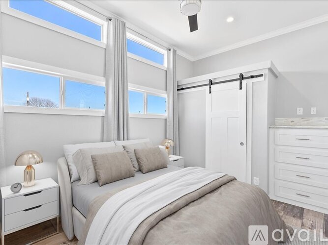 A well-lit bedroom with a large bed, a nightstand, and a window with a view of the sky.