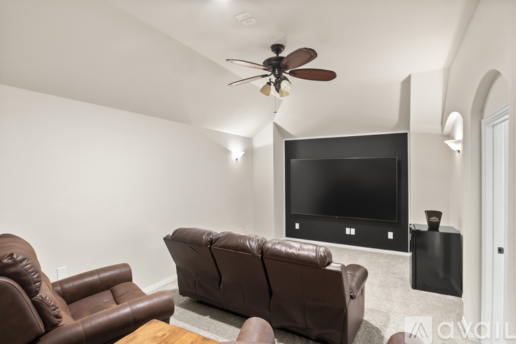 A living room with a brown leather couch and a flat screen TV mounted on the wall.