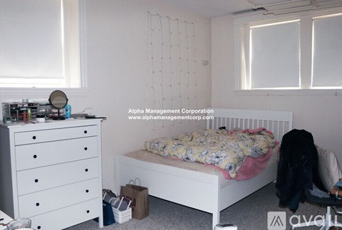 A white bedroom with a bed, dresser, and window.