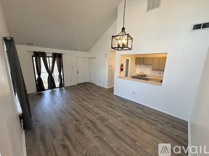 A spacious living room with a kitchen in the background and a hanging light fixture.