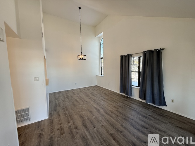 A room with wooden flooring and a window with black curtains.
