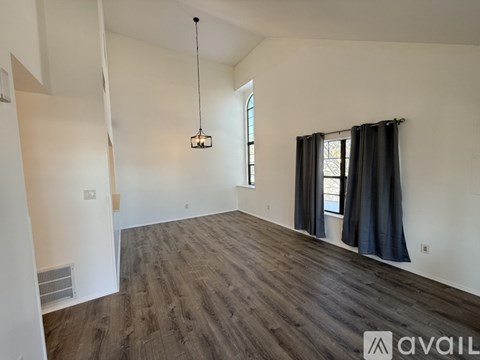 A room with wooden flooring and a window with black curtains.