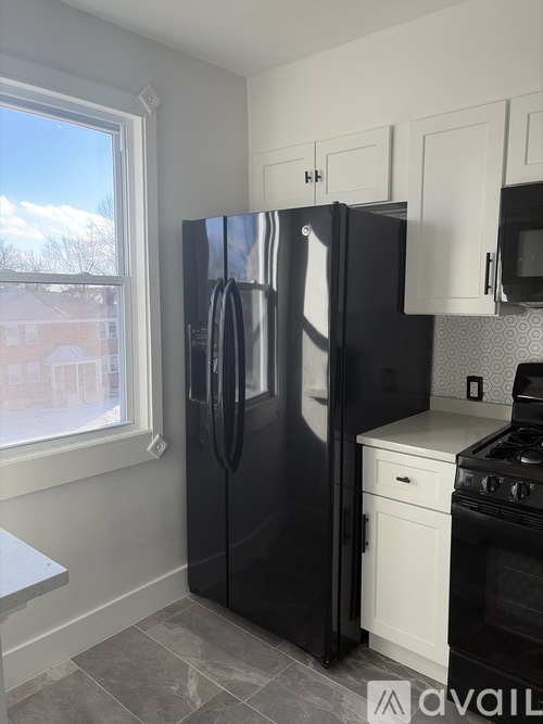 A black refrigerator in a kitchen with a window showing a view of a house.