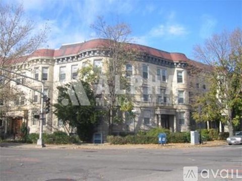 A large, old building with a red roof sits in front of a tree.