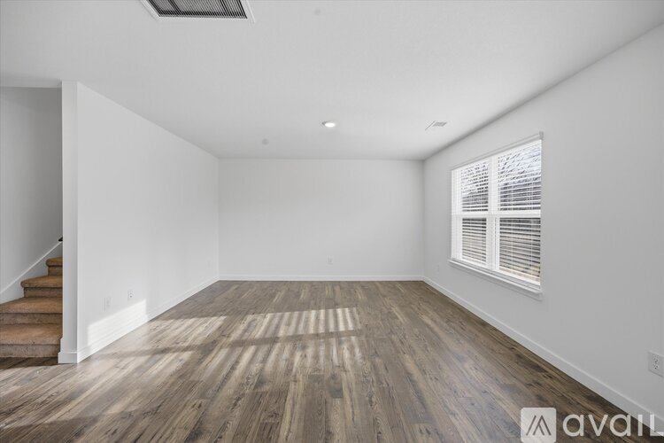 A spacious room with wooden flooring and a staircase on the left side.