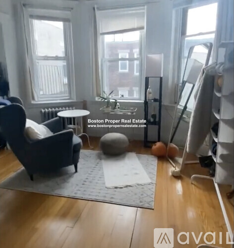 A living room with a grey rug, a grey armchair, a grey ottoman, a grey table, a grey couch, a grey chair, a grey floor lamp, a grey wall, a grey window, a grey curtain,