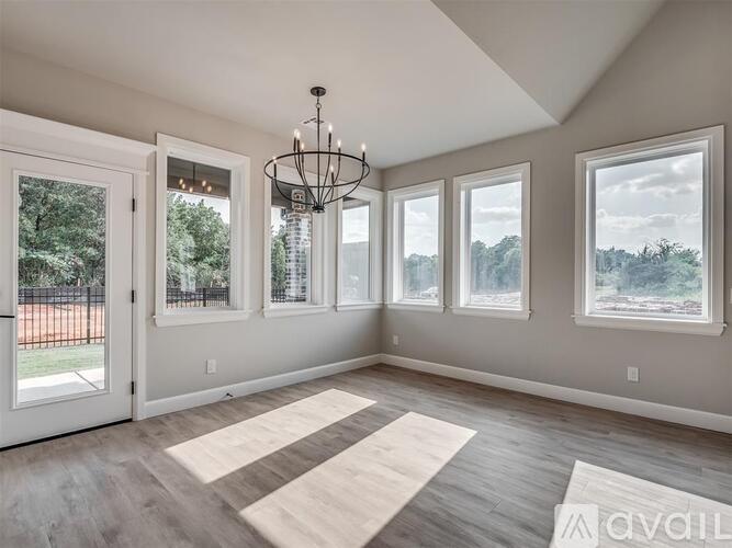 A well-lit room with a chandelier, large windows, and a view of trees and a building outside.