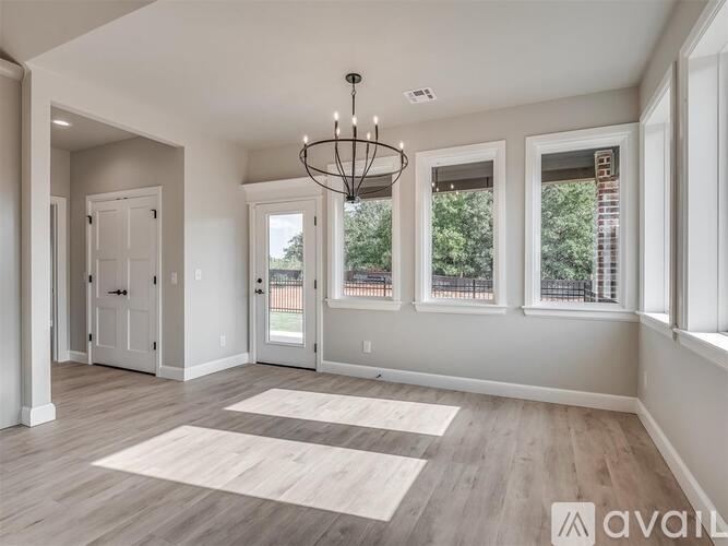 A spacious room with a chandelier, hardwood floors, and large windows.