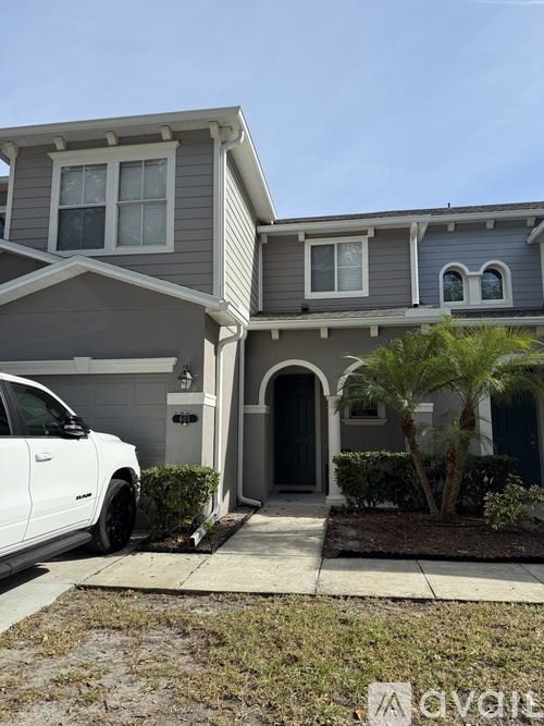 A white car is parked in front of a grey house.