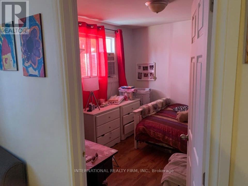 A bedroom with a bed, dresser, and window with red curtains.