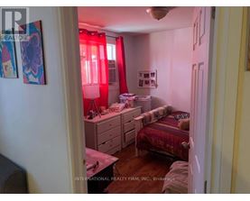 A bedroom with a bed, dresser, and window with red curtains.