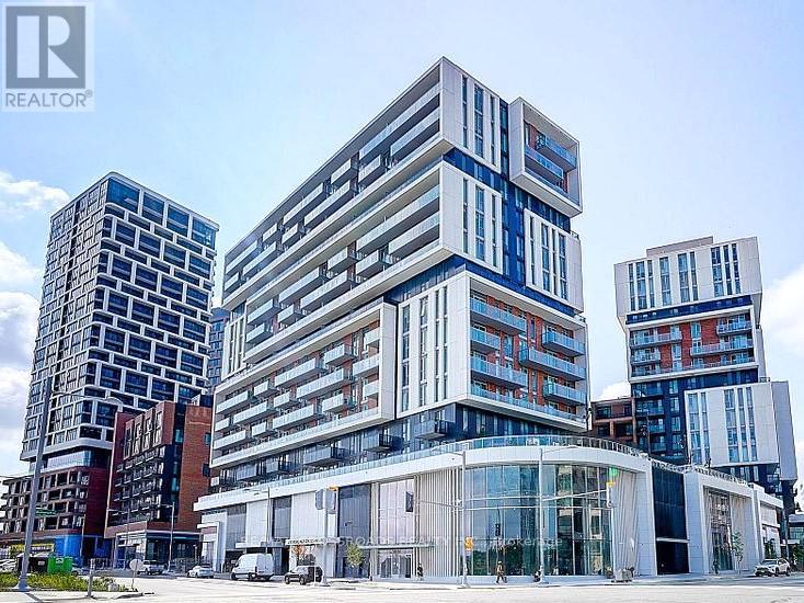 A modern multi-story building with a glass facade stands in front of other buildings.