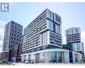 A modern multi-story building with a glass facade stands in front of other buildings.