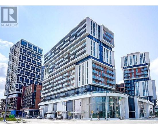 A modern multi-story building with a glass facade stands in front of other buildings.