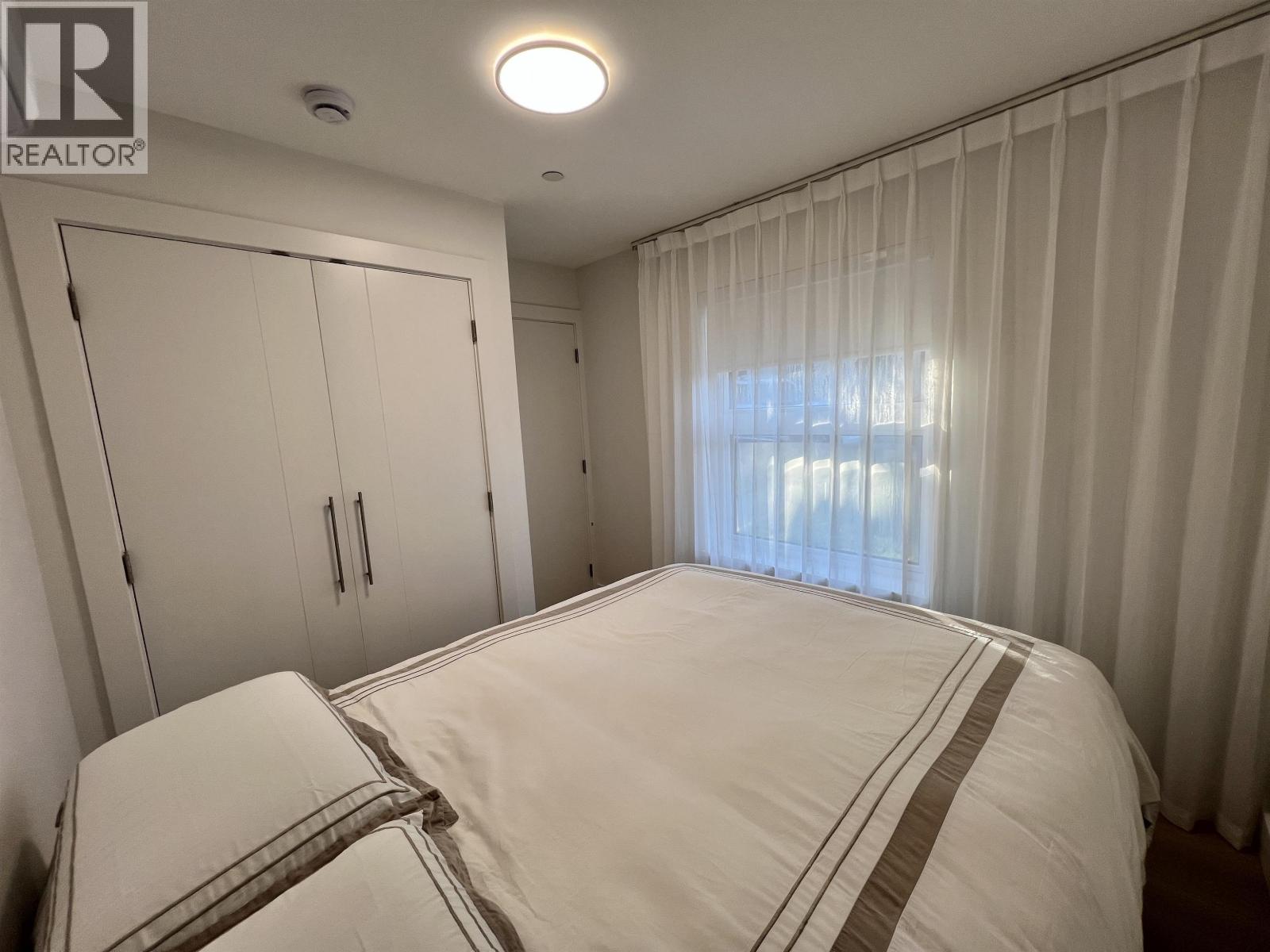 A bedroom with a large bed and a window with curtains.