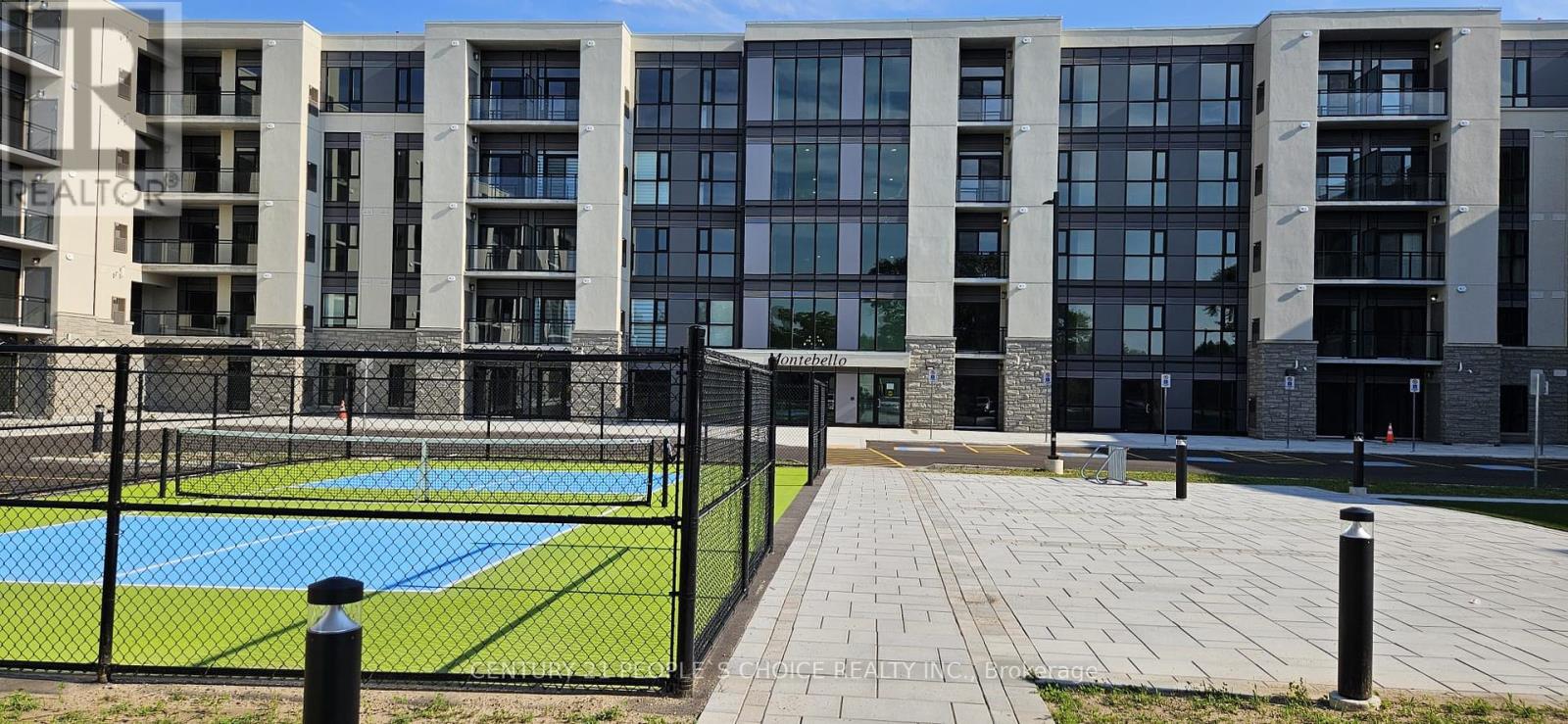 A tennis court is surrounded by a black fence and is located in front of a large building.