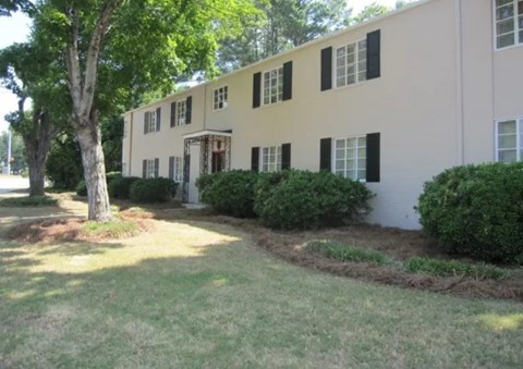 A beige building with black shutters and a tree in front.