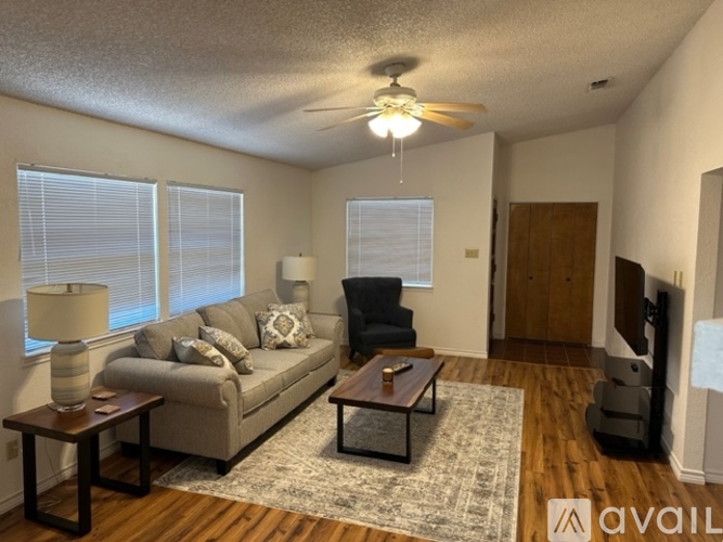 A living room with a grey couch, a coffee table, a ceiling fan, and a flat screen TV.