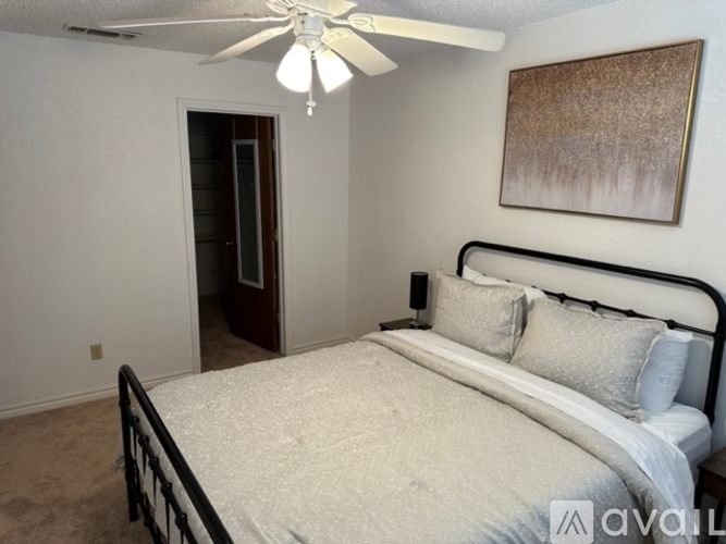 A bedroom with a bed, pillows, a ceiling fan, and a painting on the wall.
