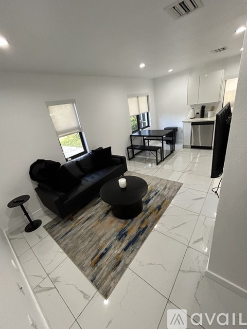 A living room with a black couch and a rug.