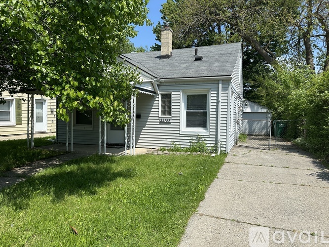 A house with a grey siding and a white window is surrounded by greenery.