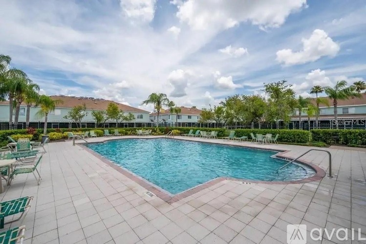 A swimming pool surrounded by a tiled patio and lounge chairs.
