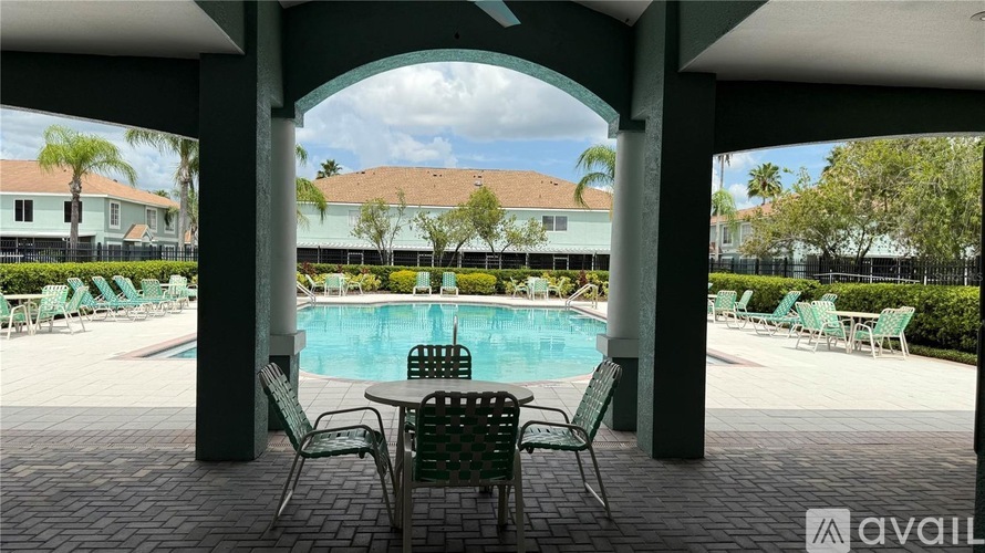 A pool area with chairs and a table under a covered area.