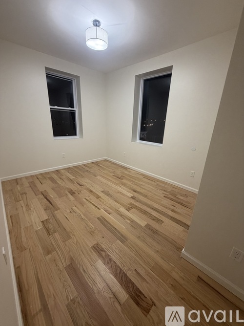 A room with wooden flooring and two windows.