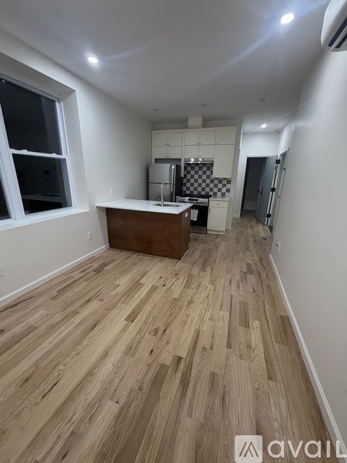 A room with wooden flooring and a kitchen area with a refrigerator, sink, and stove.