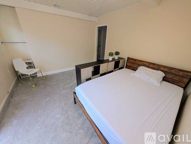 A bedroom with a bed, a chair, and a small table with a plant on it.