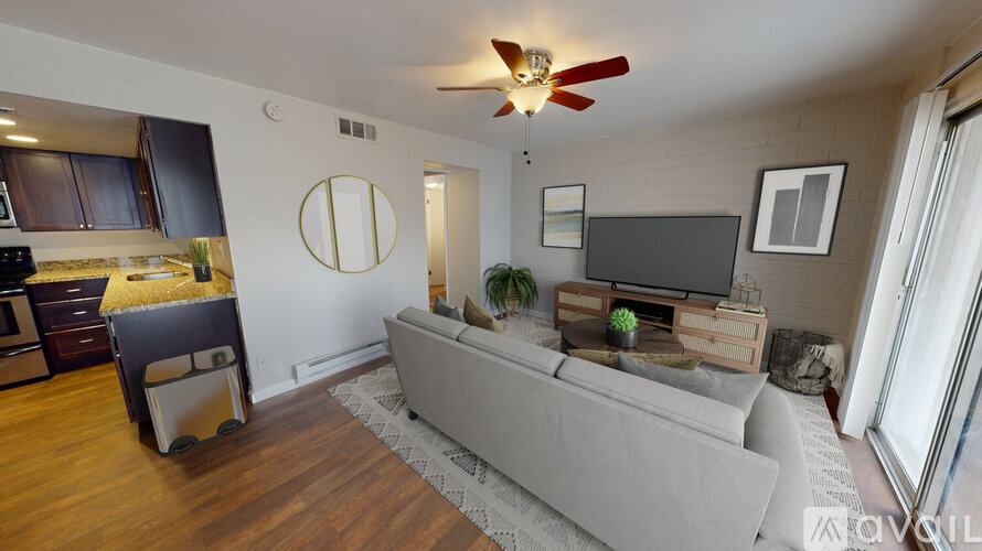 A living room with a grey couch, a wooden floor, and a ceiling fan.
