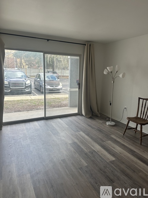 A room with a wooden floor and a sliding glass door leading to a parking lot.