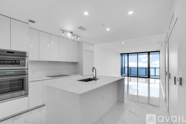 A modern kitchen with white cabinets and a large window.