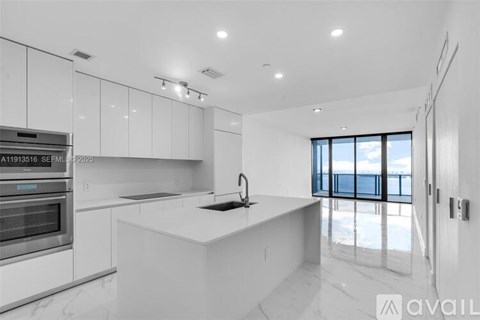 A modern kitchen with white cabinets and a large window.